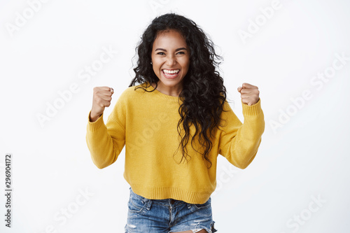 Encouraged and motivated cute african-american woman in yellow sweater raising hands up, fist pump from happiness, smiling hear good news, celebrating victory, winning huge bet, white background photo