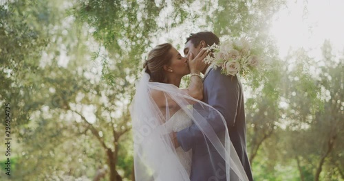 Passionate diverse couple embracing and kissing in nature on their wedding day, multi ethnic couple sharing a moment together after their marriage ceremony photo