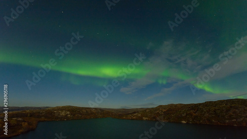 Northern lights, aurora in the sky above the hills and cliffs and reflected in the lake. © Moroshka