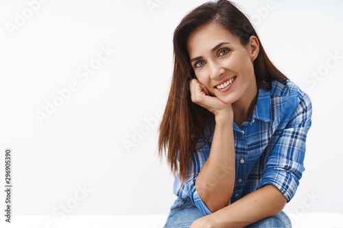Close-up lovely sensual middle-aged woman look flirty coquettish, have playful mood interesting conversation, sit table, lean face on arm smiling joyfully camera, gaze romantically, white background © Cookie Studio