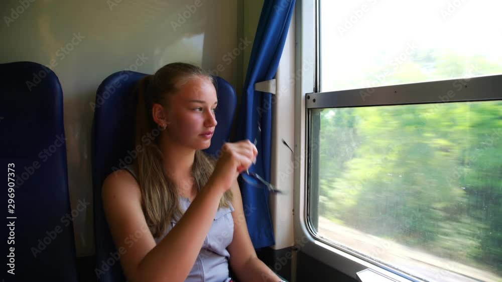 cute young girl with blonde hair in ponytail puts on sunglasses and enjoys passing landscapes outside intercity train