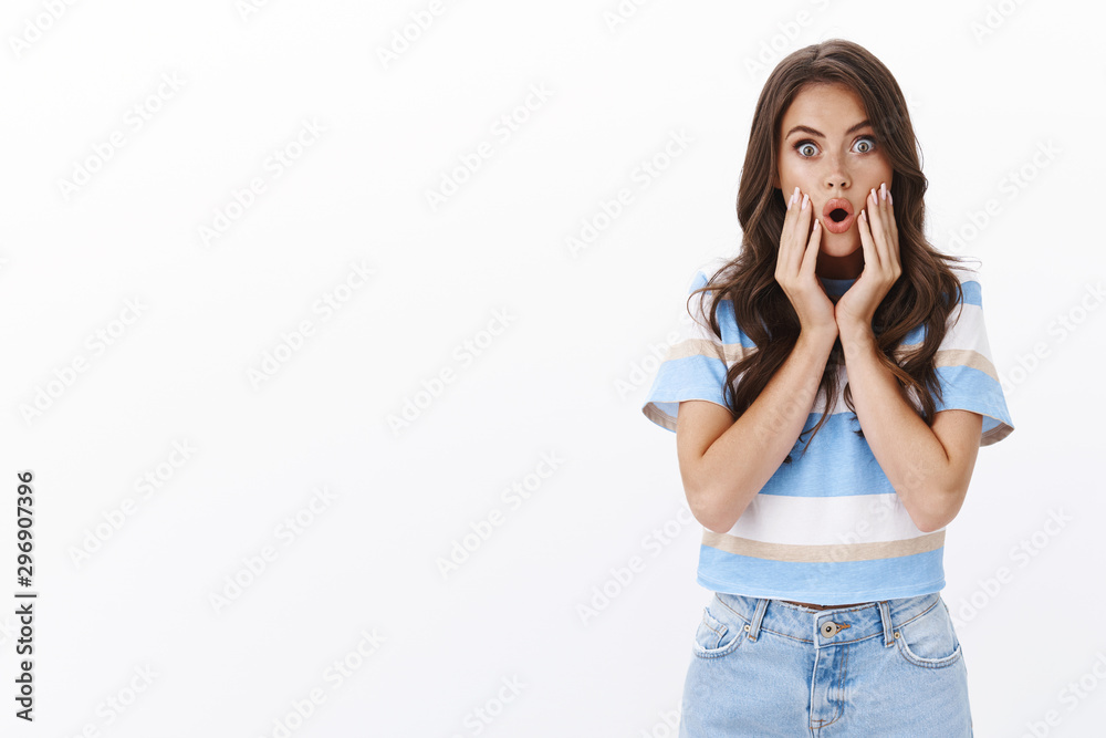 Wow awesome. Impressed european woman with long curly hairstyle, fold lips amazed and astonished, stare camera, pop eyes see unbelievable cool promo, touch face thrilled, stand white background Wow awesome. Impressed european woman with long curly hairstyle, fold lips amazed and astonished, stare camera, pop eyes see unbelievable cool promo, touch face thrilled, stand white background