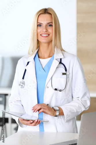 Doctor woman at work in hospital excited and happy of her profession. Blonde physician controls medication history records and exam results while using tablet computer. Medicine and healthcare concept © Iryna