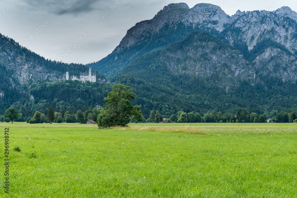 Castle of Louis II of Bavaria, the most visited monument in Germany, in the afternoon with blue and brown tones and the green meadow in the background with the sky covered with gray clouds.