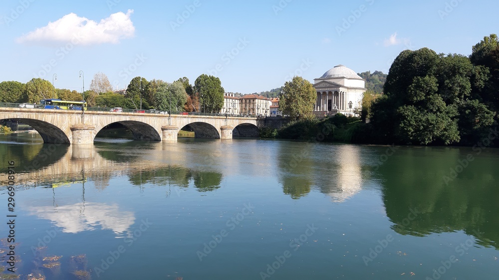 Torino, Italy - 10/17/2019: Beautiful view to the river Po, with an amazing reflection of the houses and the bridge on the water. Clear blue sky and autumn coloured trees in the background. 