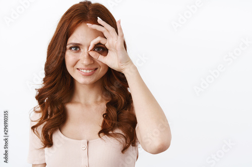 Confidence, beauty and perfection concept. Ambitious good-looking elegant young redhead woman in blouse show okay, ok sign over eye and smiling determined, standing white background assertive