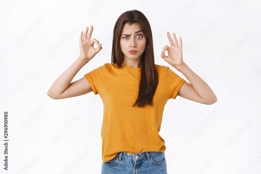 Playful, silly and cute girl in yellow t-shirt grimacing, making funny faces as showing okay, ok confirmation or approval sign, accepting something strange or weird, like it, white background Playful, silly and cute girl in yellow t-shirt grimacing, making funny faces as showing okay, ok confirmation or approval sign, accepting something strange or weird, like it, white background