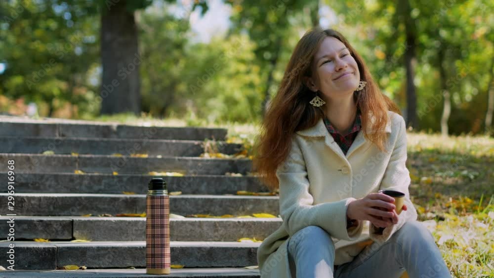 Young girl looking up, holding in hands cup of hot tea on stairs in outdoors autumn park, beautiful woman enjoy drinking cup of coffee thermos, lifestyle relax recreation weekend meditation concept Young girl looking up, holding in hands cup of hot tea on stairs in outdoors autumn park, beautiful woman enjoy drinking cup of coffee thermos, lifestyle relax recreation weekend meditation concept