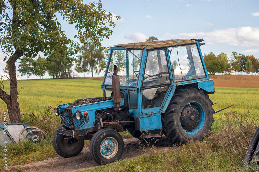 old blue tractor parked at field, sunny autumn day old blue tractor parked at field, sunny autumn day