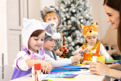 Kids with teacher make hands crafts in kindergarten. Children prepare to christmas in daycare. Group orf preschoolers on lesson in classroom