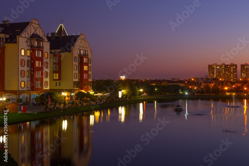 View from hill on amazing evening landscape of European village, in the center of which is lake on surface of water which reflects beautiful lights and unusual houses