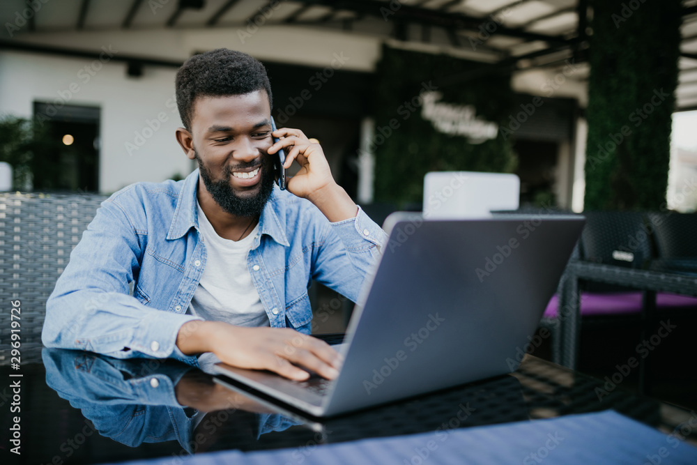Portrait of smiling african man talking on cell phone while sitting at a cafe with a laptop Portrait of smiling african man talking on cell phone while sitting at a cafe with a laptop