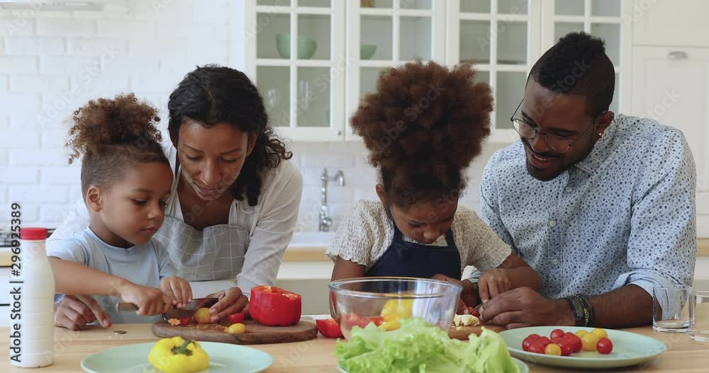Little african boy and girl helping parents cutting vegetable salad Little african boy and girl helping parents cutting vegetable salad