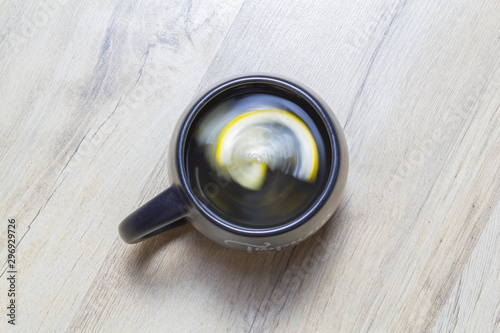 Green tea with lemon twisted in a black cup on a wooden parquet