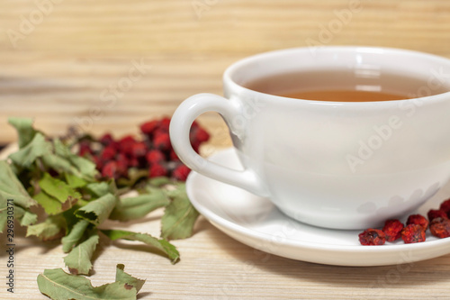 white cup of tea with plate and rowan on wooden background