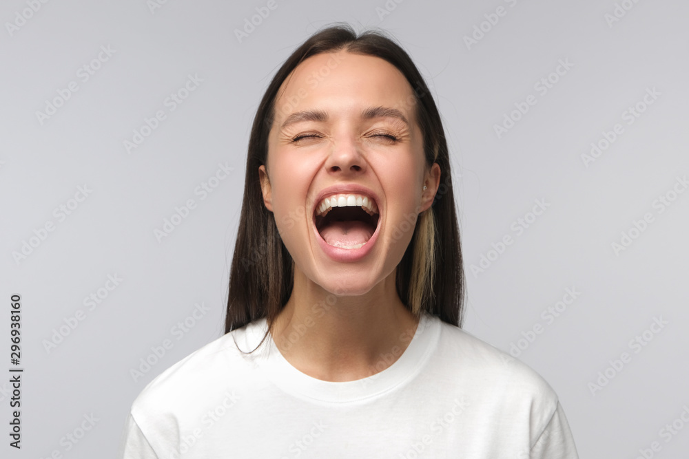 Angry woman, rage concept. Close-up portrait of screaming with closed eyes crazy young female isolated on gray background Angry woman, rage concept. Close-up portrait of screaming with closed eyes crazy young female isolated on gray background