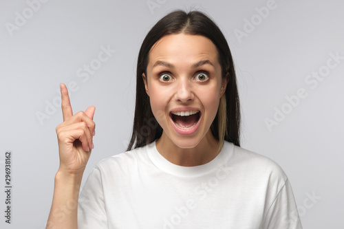 I have an idea! Young woman keeping finger pointed upwards, showing something above head, making gesture with index finger. Eureka, solution sign concept