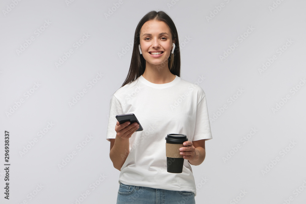 European woman looking at camera while holding phone in one hand and coffee cup in other, isolated on gray background European woman looking at camera while holding phone in one hand and coffee cup in other, isolated on gray background