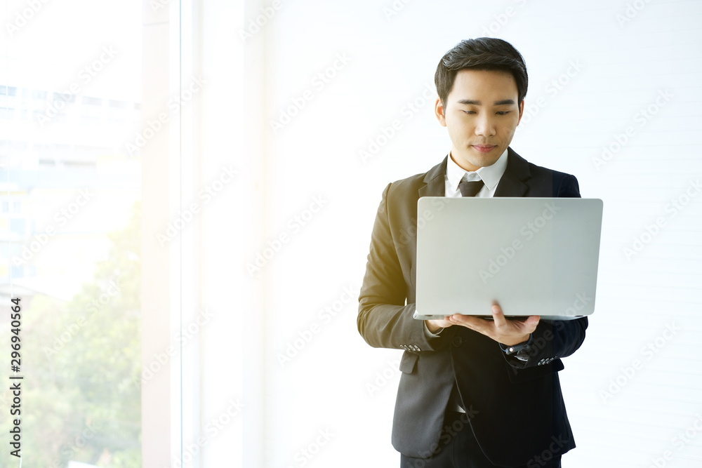 young businessman Asian wear a black suit, be a smile and standing smart poses. hold and use a computer laptop/Intelligent and confident people Successful leader / Management/ finance/ Investor. young businessman Asian wear a black suit, be a smile and standing smart poses. hold and use a computer laptop/Intelligent and confident people Successful leader / Management/ finance/ Investor.