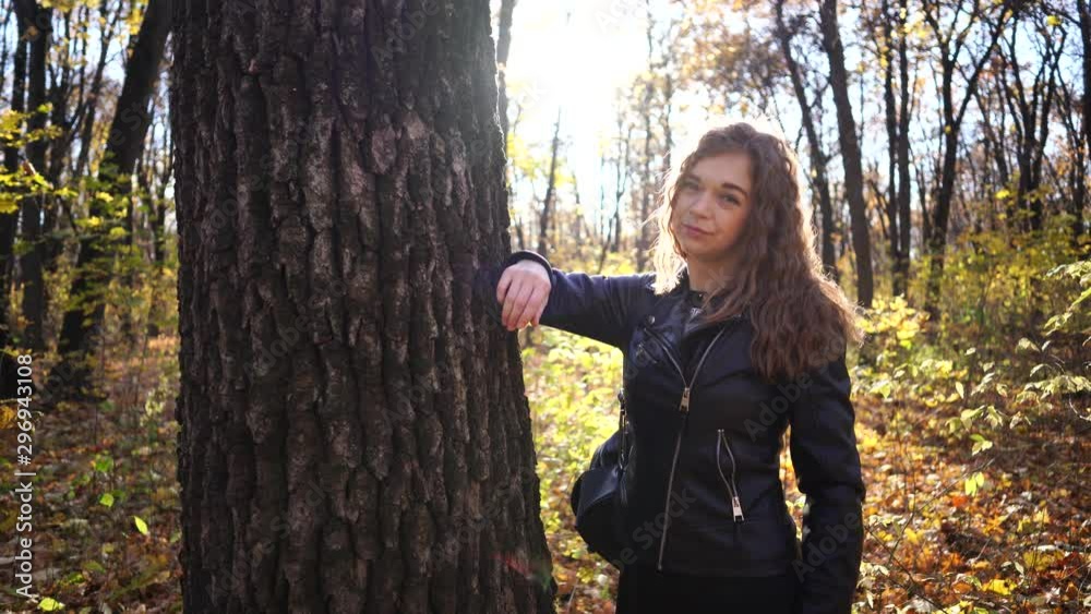 Young woman among trees. Portrait of young attractive female standing in autumn garden and looking at camera Young woman among trees. Portrait of young attractive female standing in autumn garden and looking at camera