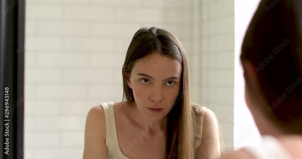 Young woman feels badly and looking at mirror at home white background Young woman feels badly and looking at mirror at home white background