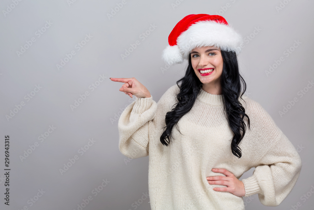 Young woman in a Santa hat pointing on a gray background