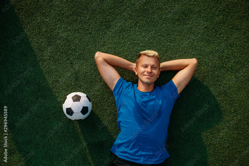 Male soccer player with ball lying on the grass Male soccer player with ball lying on the grass