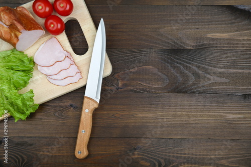 sandwich ingredients: tomato, chopped ham and lettuce on cutting board on a dark wooden background with copy space. cutting board with food and knife.