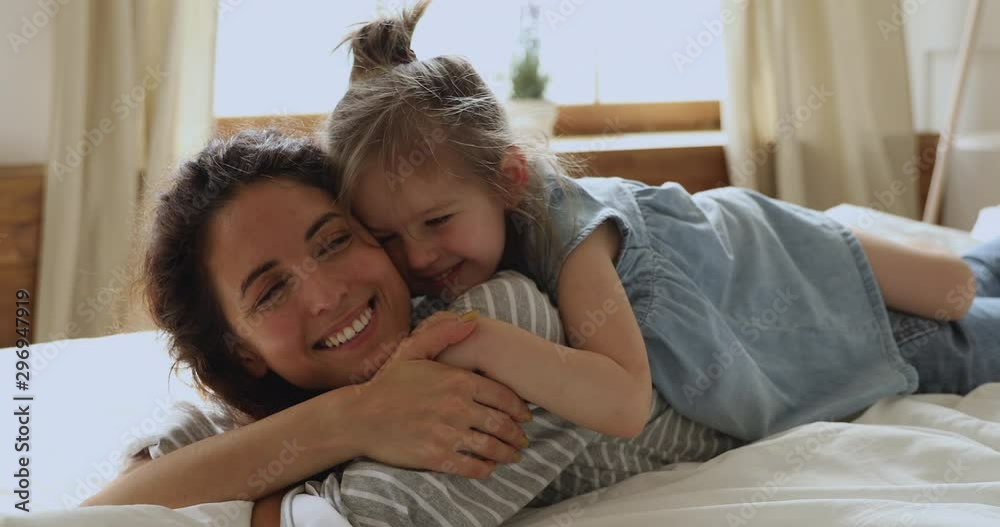 Cute little kid daughter embrace kiss mom lying on bed Cute little kid daughter embrace kiss mom lying on bed