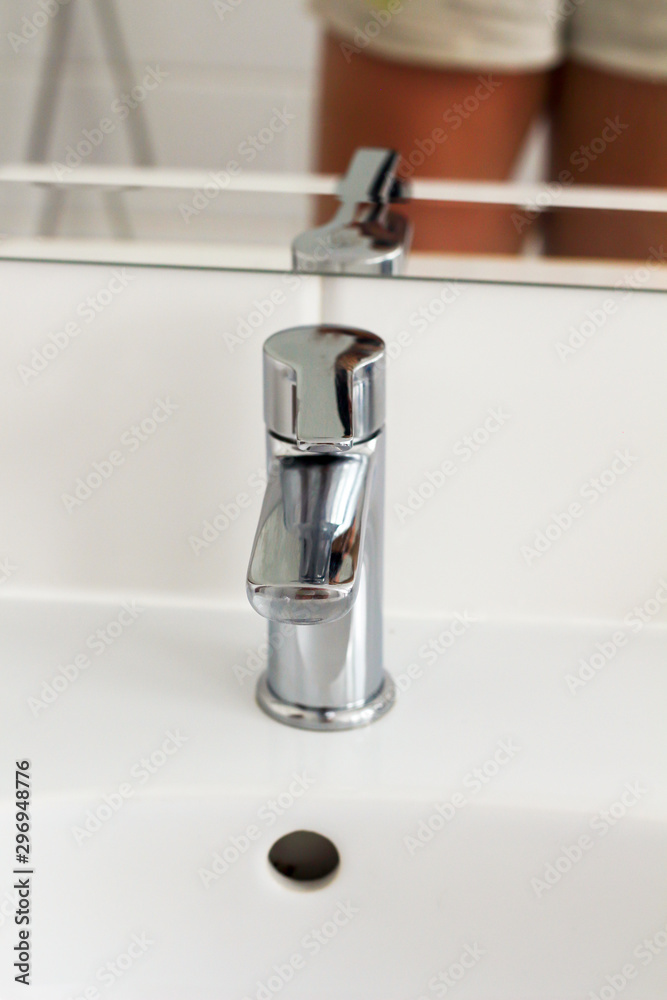 Silver metal shiny faucet water switch and ceramic sink with big mirror on background in hotel home spa bathroom with white tiles on wall. Bathroom luxury interior. Soft selective blurred focus Silver metal shiny faucet water switch and ceramic sink with big mirror on background in hotel home spa bathroom with white tiles on wall. Bathroom luxury interior. Soft selective blurred focus