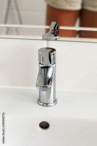 Silver metal shiny faucet water switch and ceramic sink with big mirror on background in hotel home spa bathroom with white tiles on wall. Bathroom luxury interior. Soft selective blurred focus 