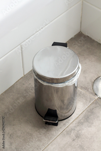 Metal silver garbage can with lid on the floor in the hotel bathroom with white tiles  on the wall. Bathroom modern luxury interior 