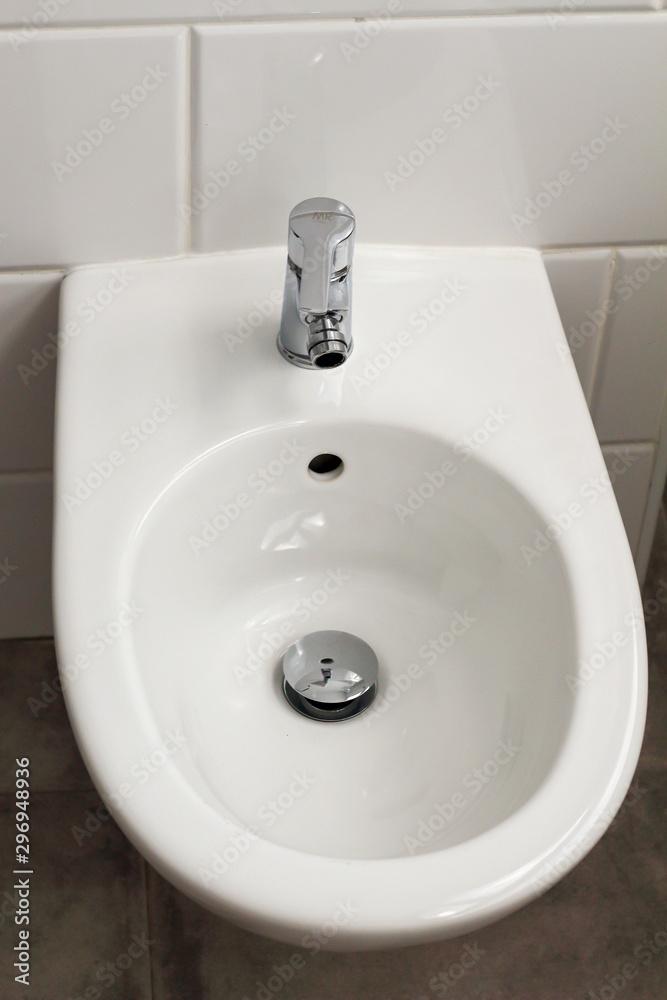 Fototapeta premium White hanging bidet seat in the hotel house bathroom with white tiles on the wall. Bathroom luxury modern interior 