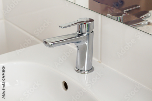 Silver metal shiny faucet water switch and ceramic sink with big mirror on background in hotel home spa bathroom with white tiles on wall. Bathroom luxury interior. Soft selective blurred focus 