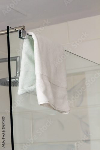 White towel hangs on a glass wall in the shower bathroom spa hotel with white tiles on the wall after washing. Luxury modern interior inside of the bathroom