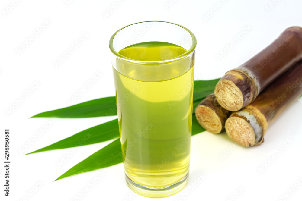Sugarcane juice in glass and pile of sugarcane beside isolated on white background.