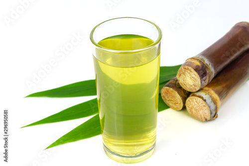 Sugarcane juice in glass and pile of sugarcane beside isolated on white background.