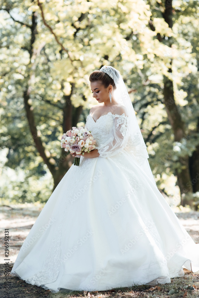 Bride holding a bouquet of flowers. Beautiful woman. Wedding bouquet in bride's hands. Beautiful bride in white dress in the park. Beautiful woman with professional make up and hair style.