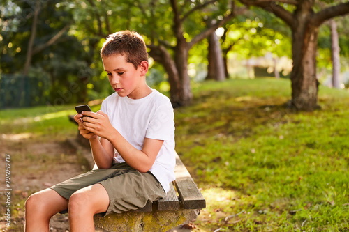 boy with a phone sits on a park bench. outdoor portrait of young boy with cell phone