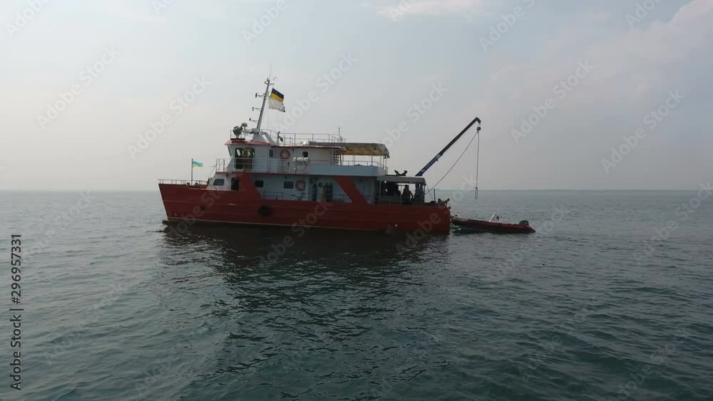 Aerial view. Fly camera a drone around red catamaran, or equipped to carry out research at sea. Rubber boat stands near stern Aerial view. Fly camera a drone around red catamaran, or equipped to carry out research at sea. Rubber boat stands near stern