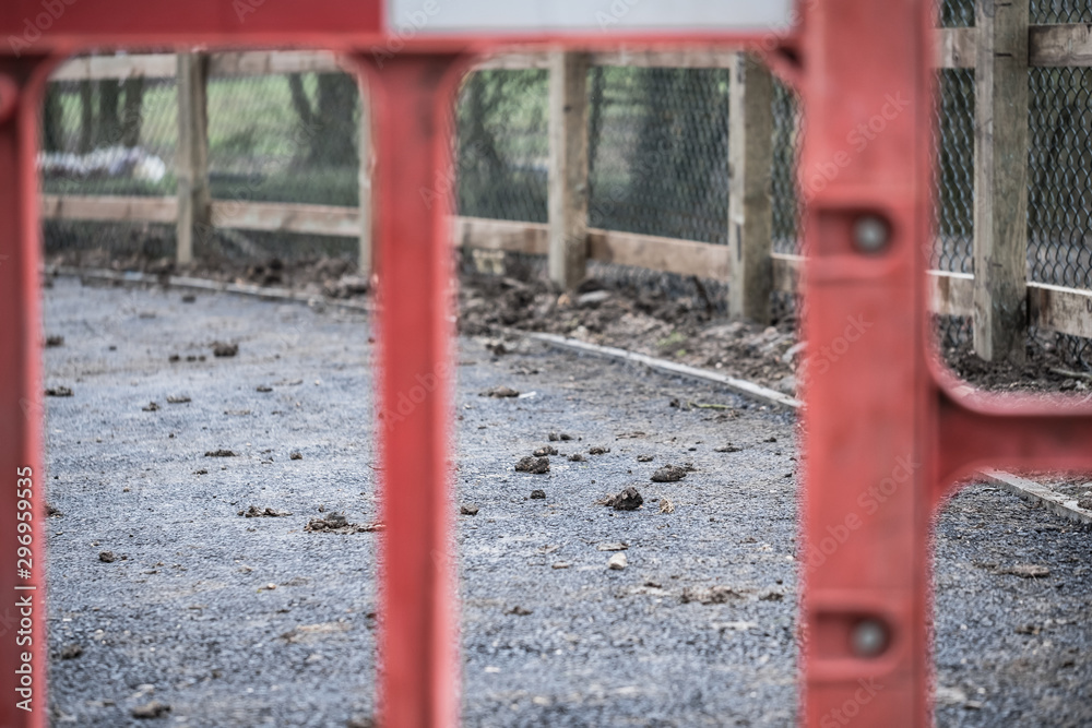Abstract view of a newly laid asphalt cycle path shown during the construction process. The foreground shows an out of focus plastic safety barrier together with a boarding wooden fence. Abstract view of a newly laid asphalt cycle path shown during the construction process. The foreground shows an out of focus plastic safety barrier together with a boarding wooden fence.