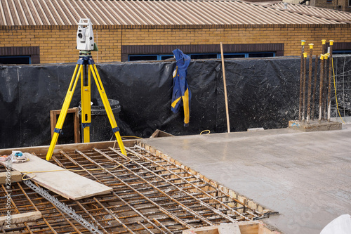 A theodolite on use on a partially cast concrete slab in a construction site. Landscape format.