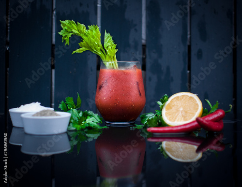 Bloody Mary cocktail in cold wet glass with celery, lemon, parsley, chilli peppers, salt and pepper on a table with a slight reflection on dark table with dark background. photo