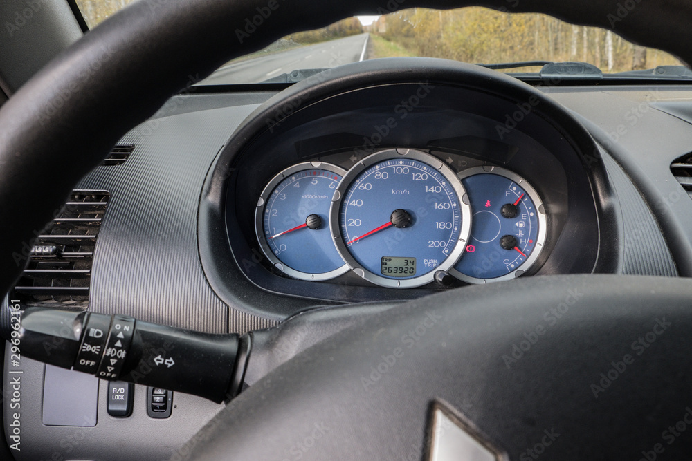 View of the dashboard and steering wheel of a car. Through the windshield you can see the road and the autumn forest. Speedometer, tachometer, fuel gauge and coolant temperature indicator. Red arrows 
