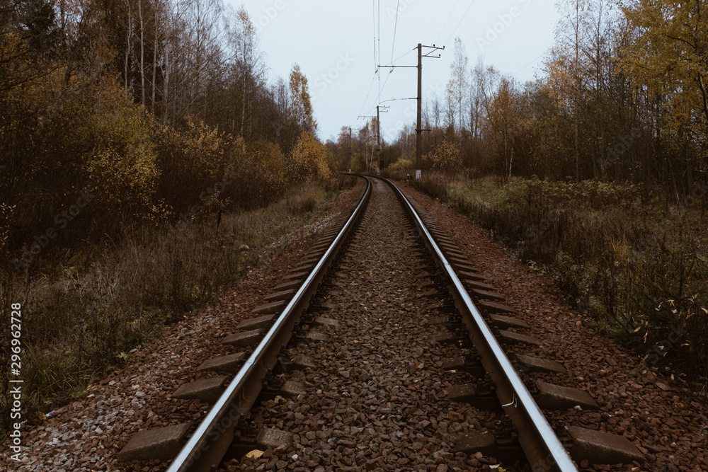 The metal rails of the railway. Reinforced concrete sleepers are covered with granite rubble. View in the autumn forest. Day. Mainly cloudy. The metal rails of the railway. Reinforced concrete sleepers are covered with granite rubble. View in the autumn forest. Day. Mainly cloudy.