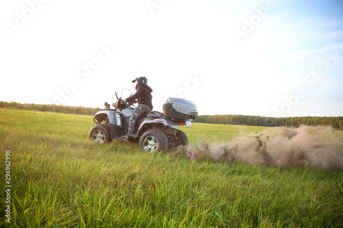 a man in a helmet rides an ATV across a field at sunset. grass and dust flies from under the wheels of the ATV.