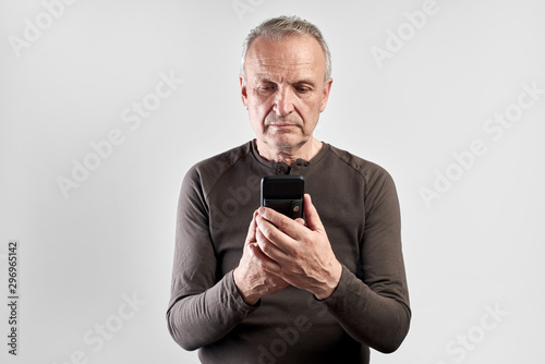Elderly handsome man with serious face looks at phone screen isolated in white studio, the older generation is mastering high technology © amixstudio