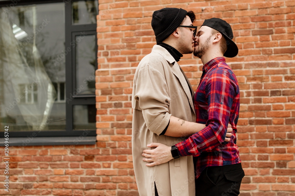 Two kissing gay men standing on the street in the background of a building