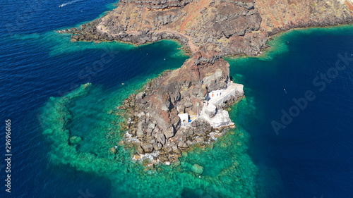 Aerial drone photo of picturesque volcanic with black rock islet and chapel of Agios Nikolaos in bay of Amoudi below iconic village of Oia, Santorini island, Cyclades, Greece