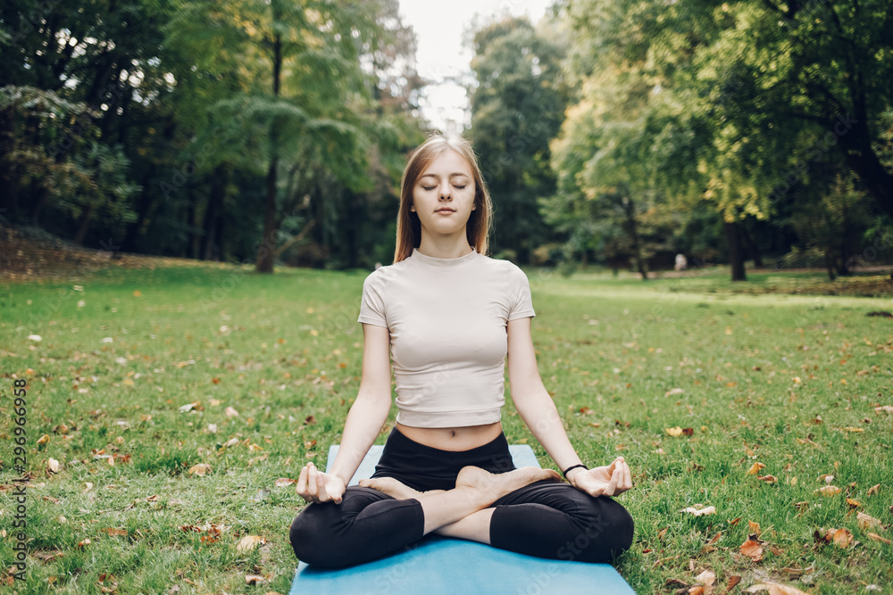  Girl meditates in lotus pose at the grass in the city park